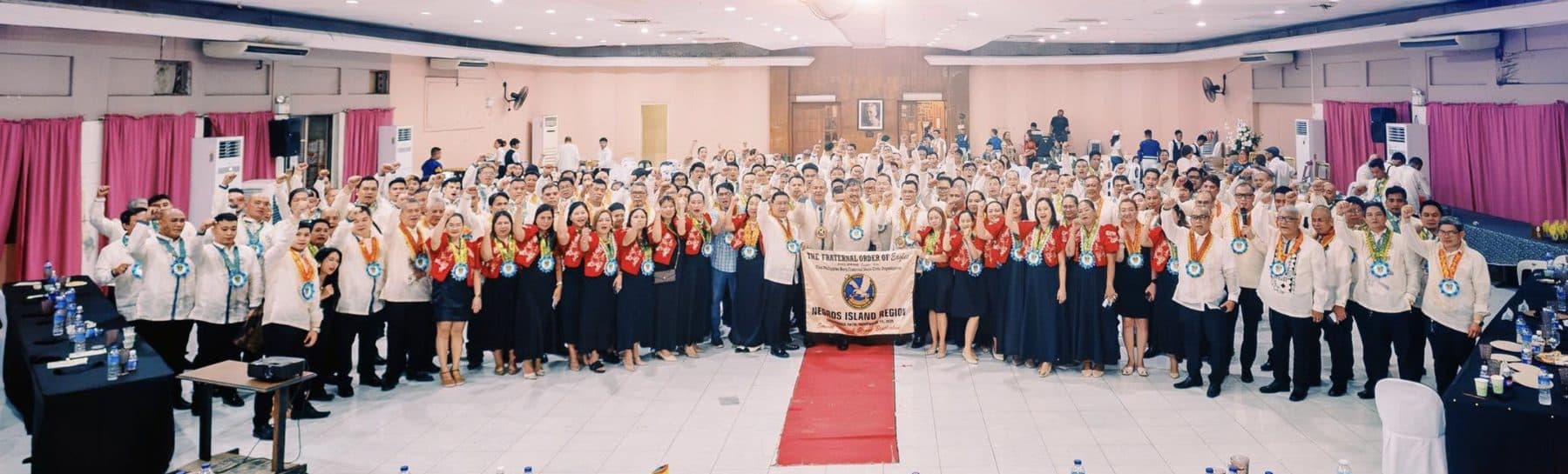 Members of the Fraternal Order of Eagles, Negros Island Region, raising their fists together at a regional gathering, holding the NIR banner